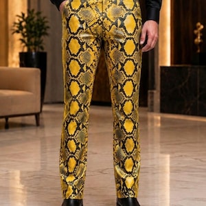 May include: Trousers featuring a vibrant yellow and black snakeskin pattern. The pants have a straight-leg cut, a standard waistband with belt loops, and a front button closure. The design displays a repeating scale texture across the entire fabric.