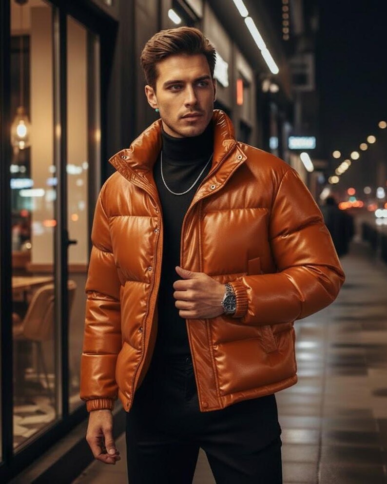 May include: A shiny, orange puffer jacket with a high collar and button closure. The jacket is worn over a black turtleneck and paired with black pants. A silver watch and chain are visible. The image is taken outdoors at night.
