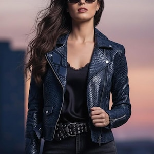 May include: A navy blue leather jacket with a snakeskin pattern, worn with a black top, jeans, and a studded belt. The jacket has a zipper closure and a classic biker style. The person is wearing sunglasses.