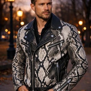 May include: A snakeskin-patterned leather jacket in black and white, featuring a black collar and zippers. The jacket has a classic biker style with a notched lapel and multiple pockets. The jacket is worn over a black shirt.