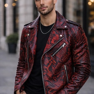 May include: A red and black snakeskin-patterned leather jacket with a classic biker style. The jacket features a notched collar, multiple zippered pockets, and a silver chain necklace. The model is wearing a black t-shirt and black pants.
