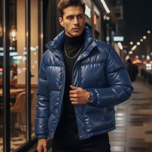 May include: A blue puffer jacket with a high collar. The jacket has a shiny, leather-like appearance and a zipper closure. The person is wearing a black turtleneck and a silver chain.