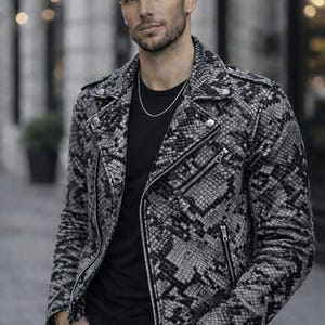 Op de afbeelding: Zwart-wit jasje met slangenprint, ritssluiting en zilverkleurige details. Het jasje wordt gedragen over een zwart t-shirt en een zwarte jeans. Een zilveren ketting is zichtbaar.