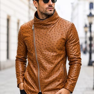 May include: A tan jacket with a textured ostrich-like pattern, featuring a high collar and an asymmetrical silver zipper closure. The garment has long sleeves and a pointed hemline, constructed with a distinct dotted surface texture throughout.