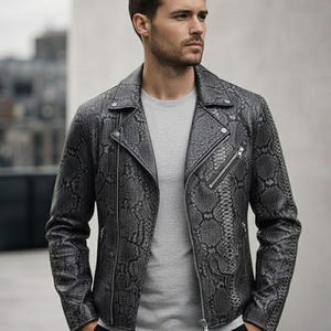 May include: A grey snakeskin-effect leather jacket in a classic biker style. The jacket has a notched collar, an asymmetrical zip, and multiple zipped pockets. The model is wearing a grey crew neck t-shirt and black trousers.