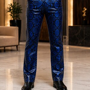 May include: Blue and black snakeskin print trousers featuring a straight-leg cut, a standard waistband with belt loops, two front pockets, and a button-fly closure. The pants are paired with a black leather belt and black leather dress shoes.