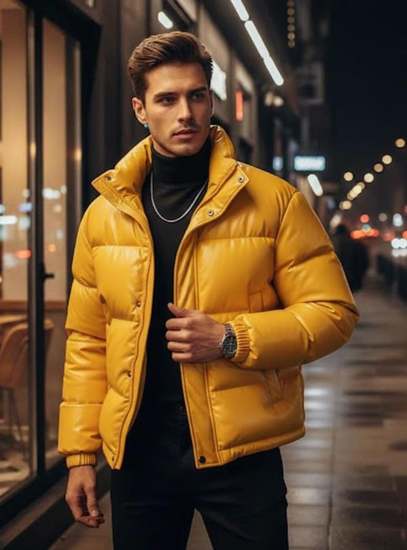 May include: A bright yellow puffer jacket with a high collar and snap closures. The jacket is worn over a black turtleneck and paired with black pants. A silver watch and chain are visible.