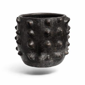 Op de afbeelding: Een donkerbruine keramische pot met een getextureerd oppervlak en talrijke afgeronde, knopachtige uitsteeksels. De pot heeft een brede opening en een licht afgeronde basis. De algehele esthetiek is rustiek en aards.