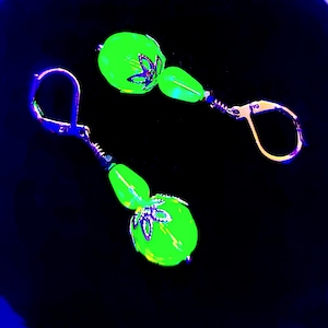 Pode incluir: Um par de brincos com contas de vidro verde e detalhes prateados. As contas são redondas e têm um design floral.