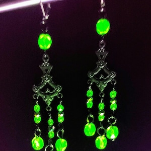 May include: A pair of dangle earrings with a silver-toned design and multiple green glass beads. The earrings are hanging from a silver-toned hook.