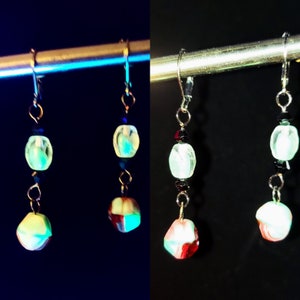 Pode incluir: Um par de brincos pendentes com uma conta preta e branca, uma conta verde claro e uma conta multicolorida. Os brincos são feitos de metal e têm um fecho de gancho.