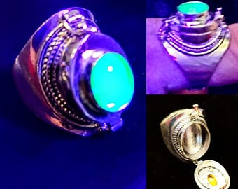 May include: A silver ring with a hinged compartment that opens to reveal a green stone. The stone glows under a black light.