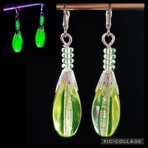 Pode incluir: Um par de brincos de gota de vidro verde com detalhes prateados. Os brincos são feitos com pequenas contas verdes e têm um design de filigrana prateada na parte inferior.