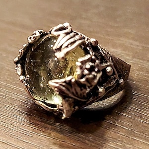 May include: A silver ring with a large, clear, yellow-green gemstone set in a detailed, ornate, silver setting.