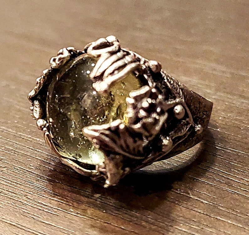 May include: A silver ring with a large, clear, yellow-green gemstone set in a detailed, ornate, silver setting.