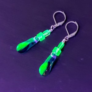 Pode incluir: Um par de brincos de prata com contas de vidro verde em forma de lágrima e contas quadradas.