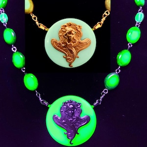 Könnte beinhalten: Eine grüne Glaskette mit zwei runden Anhängern, die ein Frauenbild in Relief zeigen. Der obere Anhänger ist golden und der untere Anhänger ist silbern.