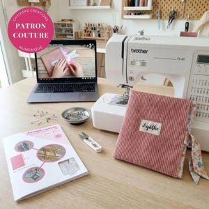 May include: A white Brother FS40 sewing machine sits next to a laptop displaying a sewing tutorial, a small metal bowl of pins, a seam ripper, a printed instruction booklet, and a pink corduroy fabric cover with a label reading Agathe.