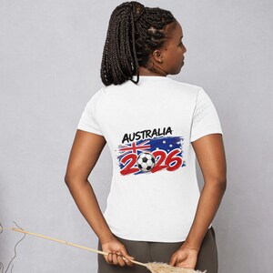 May include: White t-shirt with the text "AUSTRALIA 2026" in red and blue, featuring a soccer ball and the Australian flag. The shirt is short-sleeved and has a crew neck.