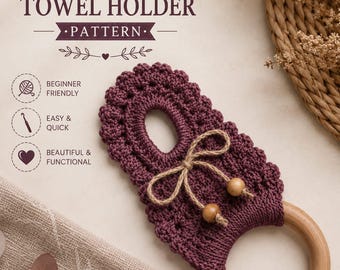 May include: A crochet cabinet knob towel holder pattern featuring a dark plum-colored crocheted piece with a scalloped edge, a central opening, and a natural wooden ring. The design includes a jute twine bow with two wooden beads attached.