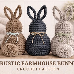 May include: Three handmade crochet bunny figurines in brown, navy blue, and gray. Each bunny has a pom-pom tail and a decorative bow. The text "RUSTIC FARMHOUSE BUNNY CROCHET PATTERN" is at the bottom.