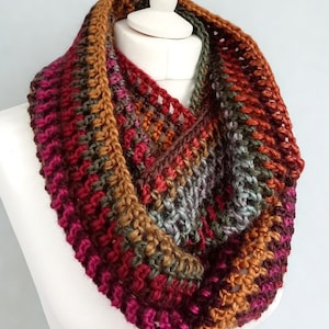 Peut inclure: Écharpe-cowl multicolore faite à la main, présentée sur un mannequin blanc. Elle présente un mélange de couleurs chaudes, notamment des nuances de rouge, d'orange, de marron et de vert. La texture tricotée est visible, mettant en valeur le savoir-faire. Accessoire idéal pour l'hiver.