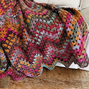 Può includere: Una coperta lavorata all'uncinetto a mano con un vivace motivo a piastrelle granny in una tavolozza multicolore di magenta, arancione, verde oliva, azzurro e viola scuro. Il tessuto presenta una superficie testurizzata e annodata con bordo smerlato.