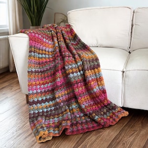 Può includere: Una coperta all'uncinetto caratterizzata da un motivo a punti ripetuti e testurizzati in una vivace tavolozza di colori magenta, arancione, giallo senape, verde acqua e marrone scuro. Il filato presenta un aspetto variegato.