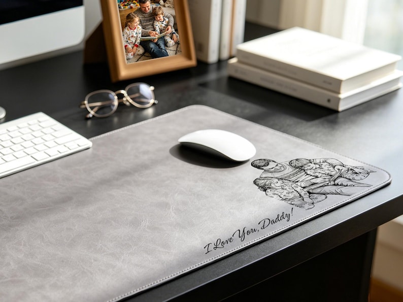 May include: A rectangular gray desk mat with a smooth, textured surface. The mat features a black line-art illustration of a parent and two children, accompanied by the printed text "I Love You, Daddy!" in a cursive script font on the lower right side.