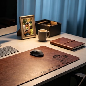 May include: A brown leather desk mat featuring an engraved illustration of an adult and a child embracing, with the text "I Love You, Daddy!" etched into the surface. The mat is positioned on a desk with a computer keyboard, a mouse, and a photo frame.