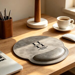 May include: A round gray mouse pad with a built-in wrist rest. The surface features a black printed design with a large letter H, the name Harvey, the phrase My love, and the date 5.26.2025. The mouse pad has a textured finish and stitched edges.