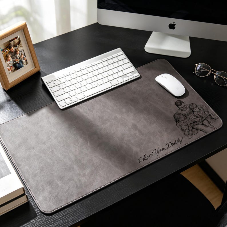 May include: A grey leather desk mat with a stitched border. The mat has a family portrait and the text "I Love You, Daddy!". A white keyboard and mouse are on the mat, with a framed photo and computer monitor in the background.