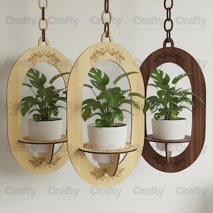 May include: Three hanging wooden planters with oval frames and decorative floral cutouts. Each planter holds a green plant in a white pot. The planters are suspended by brown chains. The word "Crafty" is visible.