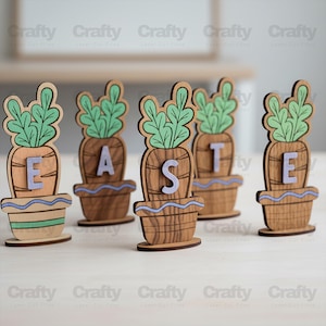 Puede incluir: Decoraciones de Pascua de madera que deletrean "EASTE". Cada decoración presenta un diseño de zanahoria con copas verdes y una letra morada clara. Las zanahorias están colocadas en macetas decorativas con detalles azules.