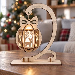 May include: A light-colored wooden decorative lamp featuring a cat-shaped silhouette with a bow at the top. A hanging lantern with intricate laser-cut panels depicting deer and forest trees is suspended from the cat's tail, illuminated by a warm light.