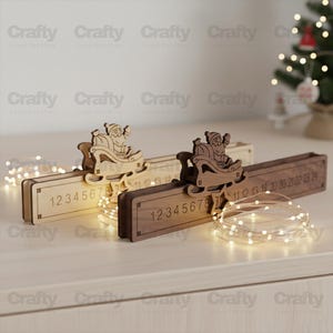 Puede incluir: Dos calendarios de adviento rectangulares de madera, uno claro y otro oscuro, cada uno con un adorno de Papá Noel en trineo cortado con láser y los números del 1 al 24 grabados en la parte frontal, acompañados de finas luces de cadena.