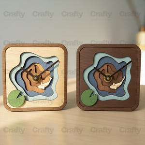 Puede incluir: Dos relojes cuadrados de madera con un diseño en capas que representa un estanque de carpas koi. Los relojes presentan un acabado en madera clara y oscura, con detalles en azul, marrón y verde. Las manecillas del reloj son negras y la esfera tiene un diseño de pez koi.
