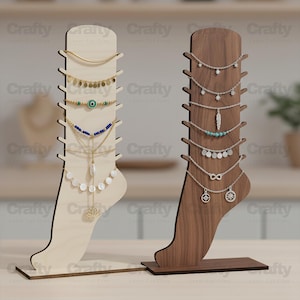 May include: Two vertical foot-shaped jewelry display stands made of wood. The left stand is light-colored wood, and the right stand is dark-colored wood. Each stand features multiple side notches for hanging necklaces or anklets, which are currently displayed.