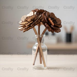May include: A clear glass vase holds three wooden flowers with brown petals and stems. The flowers are intricately designed with layered petals, creating a three-dimensional effect. The vase sits on a light-colored surface.
