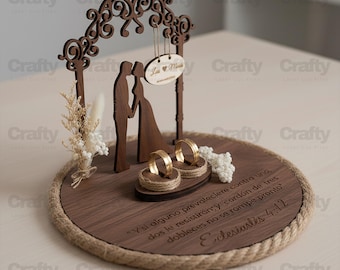 May include: A wooden wedding ring holder with a decorative arch, bride and groom silhouettes, and two gold rings. The holder includes a small sign with names and a Bible verse. The base is round with a rope border.