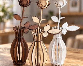 May include: Three laser-cut wooden rose sculptures in dark brown, light tan, and white, each standing in a matching slotted wooden vase. The flowers feature layered petals, a single stem, and two leaves, all constructed from flat, interlocking wood pieces.