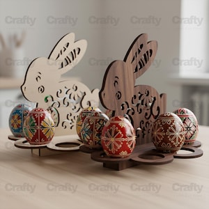 Könnte beinhalten: Zwei hölzerne Osterhasen-Eierhalter, einer hell und einer dunkel, jeweils mit dekorativen Ausschnitten. Sie zeigen gemusterte Ostereier in verschiedenen Farben. Die Eier haben komplizierte Designs. Auf einer Holzoberfläche.
