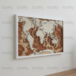 May include: A rectangular wall art piece featuring a multi-layered wooden world map with a white frame. The map displays continents in light wood tones set against a darker, reddish-brown wood background, creating a three-dimensional depth effect.