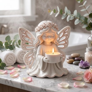 May include: A white ceramic angel figurine with a floral crown and detailed wings, holding a lit candle. The angel has closed eyes and is surrounded by rose petals and eucalyptus leaves. The candle holder is approximately 2 inches in diameter.