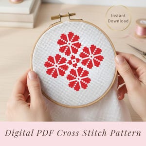 Può includere: Un motivo a punto croce in un telaio da ricamo in legno. Il design presenta una disposizione simmetrica di motivi floreali rossi su tessuto bianco. Le parole "Download istantaneo" sono in un cerchio dorato. Il testo "Digital PDF Cross Stitch Pattern" è in basso.