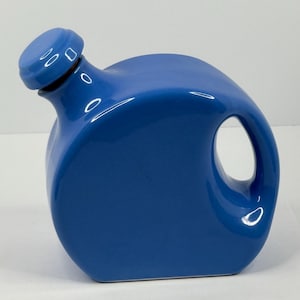 May include: A blue ceramic pitcher with a rounded body and a handle. The pitcher has a spout with a matching blue lid. The design is modern and minimalist, with a glossy finish. The pitcher is likely used for serving beverages.