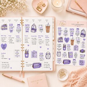 May include: A planner open to a weekly spread featuring purple faith-themed stickers, alongside a matching sticker sheet, a pink pen, and a small notebook. The stickers include illustrations of books, a backpack, a coffee cup, and an alarm clock.