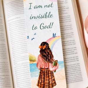 May include: Bookmark with the text "I am not invisible to God!" featuring a watercolour illustration of a person looking at a rainbow over the ocean. The bookmark is placed in an open book.