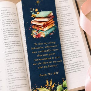 May include: Dark blue bookmark featuring a stack of illustrated books in green, orange, and brown. The bookmark has the text "Be thou my strong habitation..." from Psalm 71:3 KJV. The bookmark is in an open book.