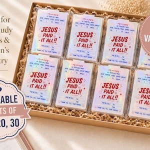 May include: A cardboard box filled with seven rectangular cards in clear plastic sleeves. Each card features a holographic finish and red text that reads: Jesus Paid It All, along with fields for book, chapter, verse, and a thank you message.